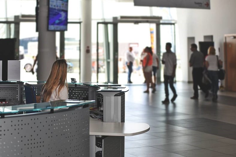 3 Reasons To Upgrade Your Office Flooring In 2024 2 A receptionist looking at people in the background walking on a grey tiled floor.