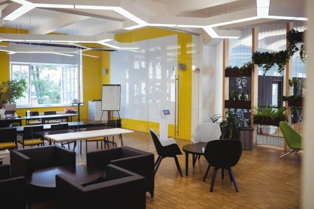 3 Ways To Protect Your Commercial Flooring During The Summer 2 A modern open office plan with black furniture, yellow walls, and wooden flooring.